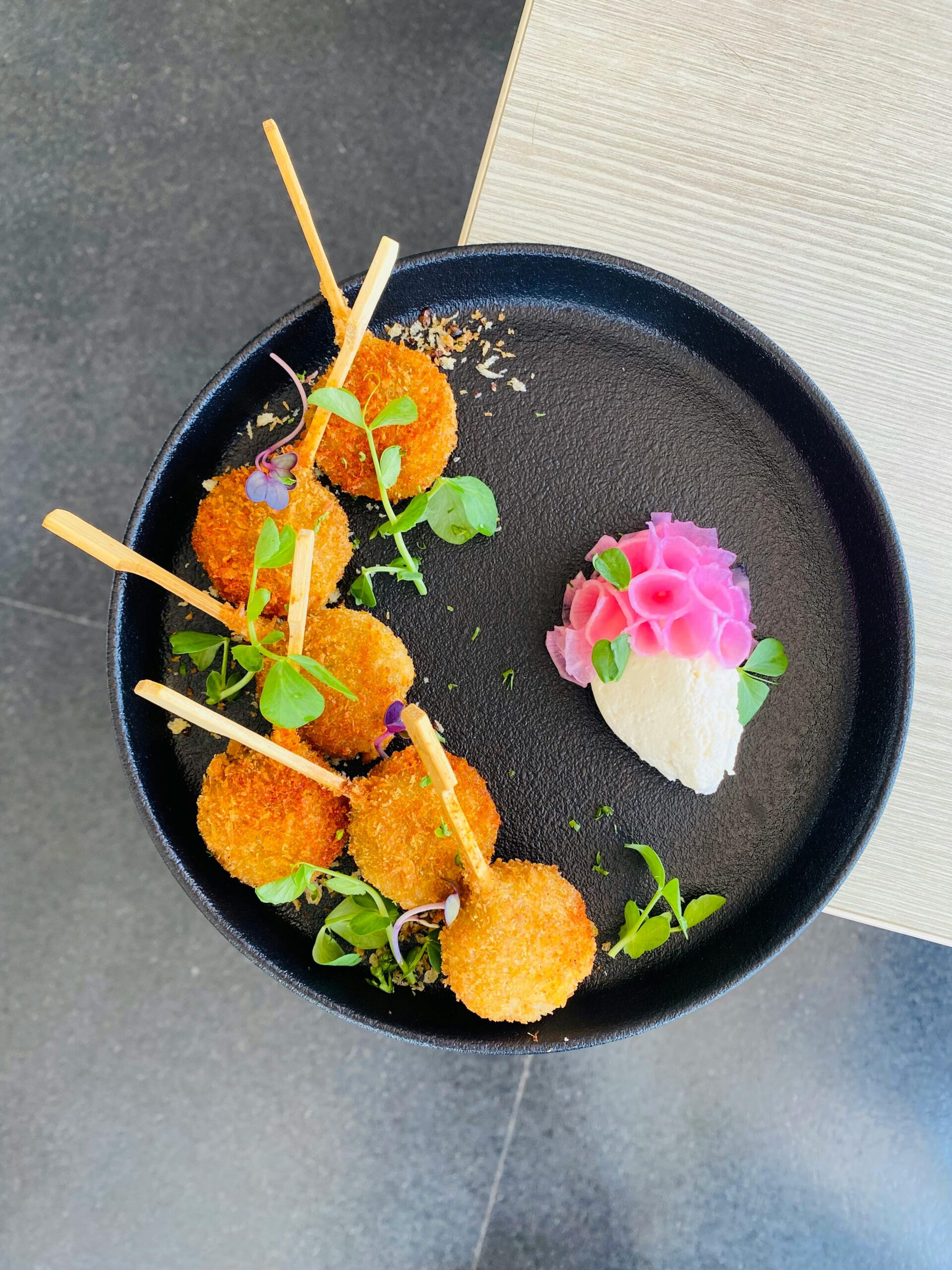 Delicious crispy fried snacks served on a black plate with fresh garnish and pink vegetable rose.